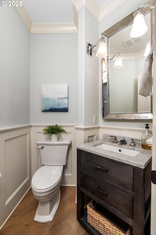 bathroom featuring ornamental molding, wood finished floors, wainscoting, vanity, and toilet