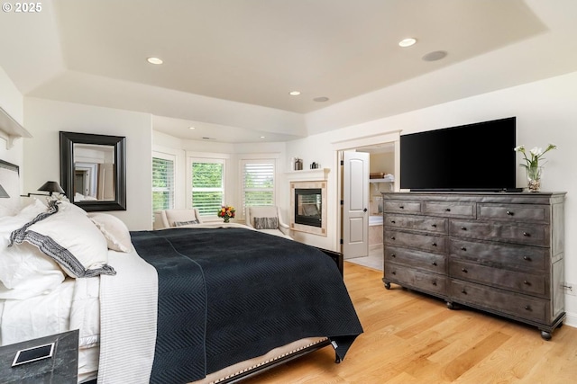 bedroom featuring light wood finished floors, a raised ceiling, a multi sided fireplace, and recessed lighting