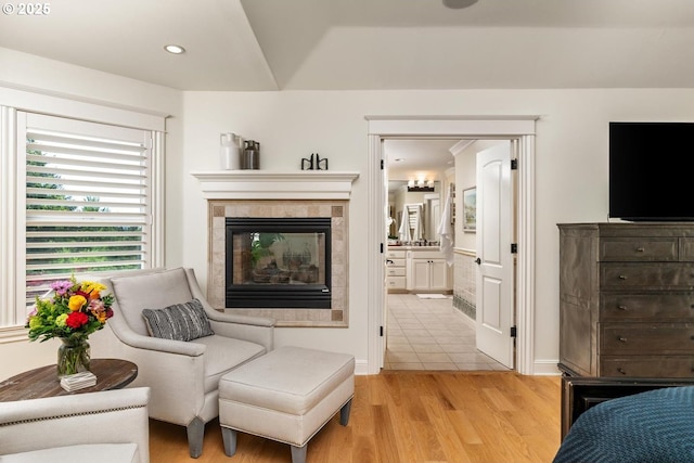 bedroom with a tiled fireplace, light wood-type flooring, connected bathroom, recessed lighting, and baseboards