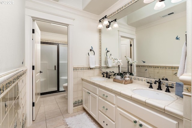 bathroom with tile walls, tile patterned flooring, a stall shower, double vanity, and a wainscoted wall