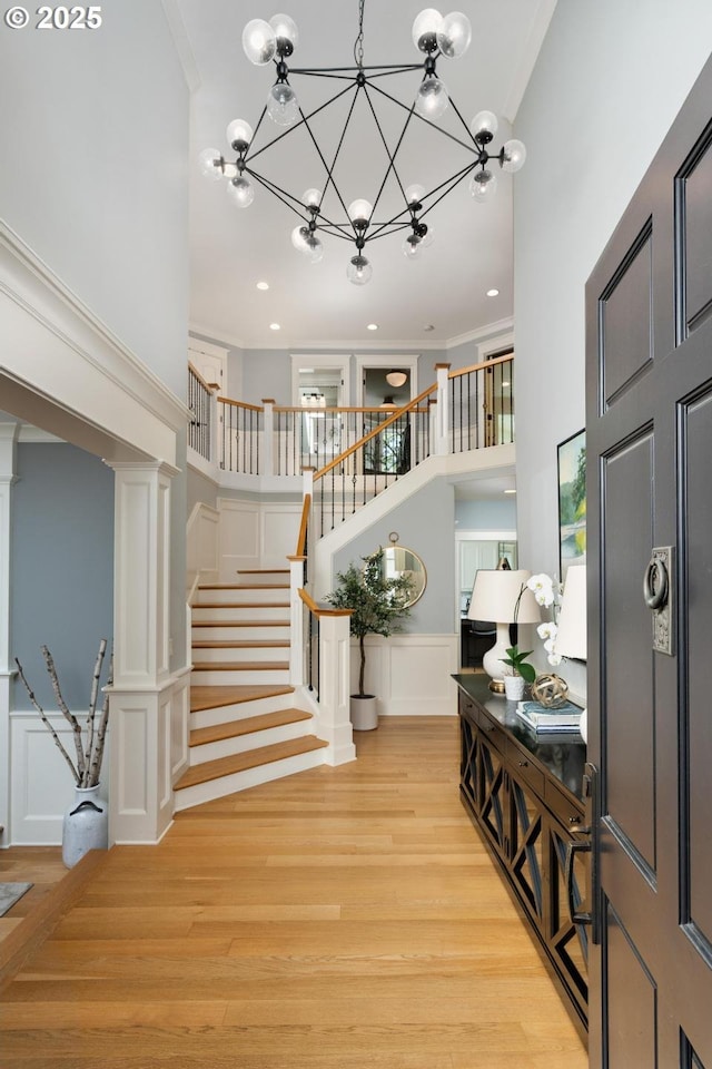entryway featuring a towering ceiling, a chandelier, stairway, light wood-style flooring, and crown molding