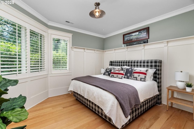 bedroom with a decorative wall, wood finished floors, and ornamental molding