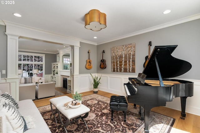 living room featuring decorative columns, light wood-style flooring, a wainscoted wall, crown molding, and recessed lighting