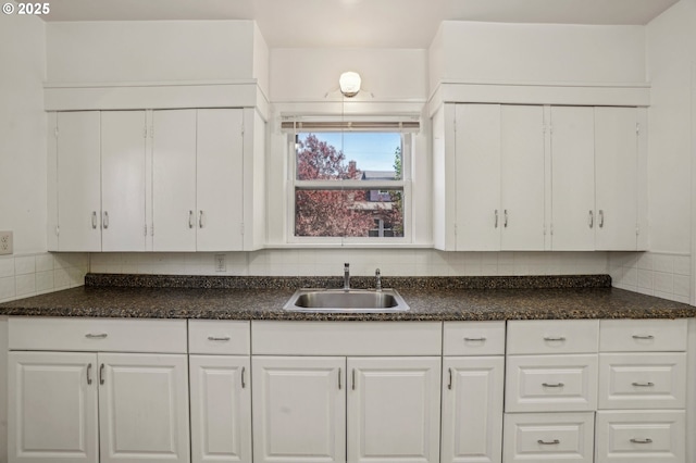 kitchen featuring a sink, decorative backsplash, white cabinets, and dark countertops