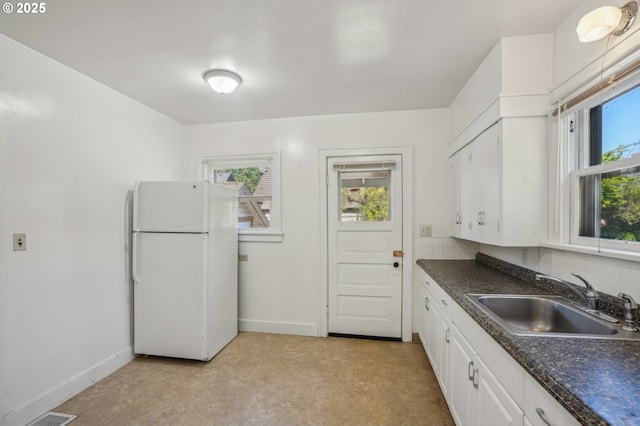 kitchen with dark countertops, a sink, baseboards, freestanding refrigerator, and white cabinetry