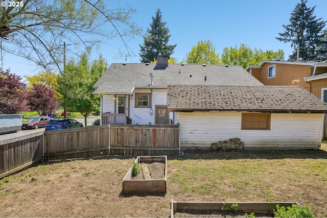 back of house featuring a lawn, a shingled roof, fence, and a vegetable garden