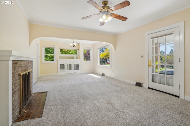 unfurnished living room featuring crown molding, carpet floors, arched walkways, a brick fireplace, and baseboards