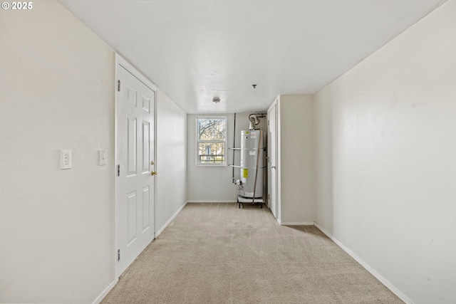 empty room with gas water heater, light colored carpet, and baseboards