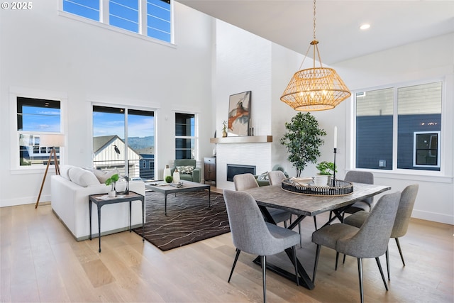 dining space featuring a notable chandelier, a towering ceiling, a fireplace, and light hardwood / wood-style floors