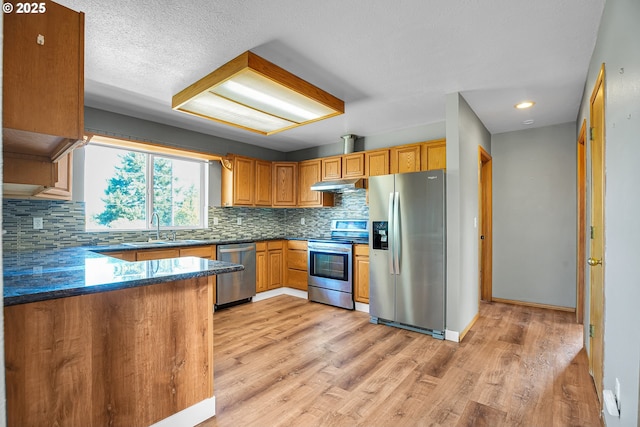 kitchen featuring appliances with stainless steel finishes, a sink, decorative backsplash, dark countertops, and light wood-style flooring