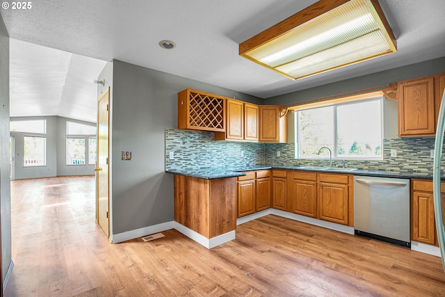 kitchen featuring stainless steel dishwasher, a sink, healthy amount of natural light, dark countertops, and vaulted ceiling