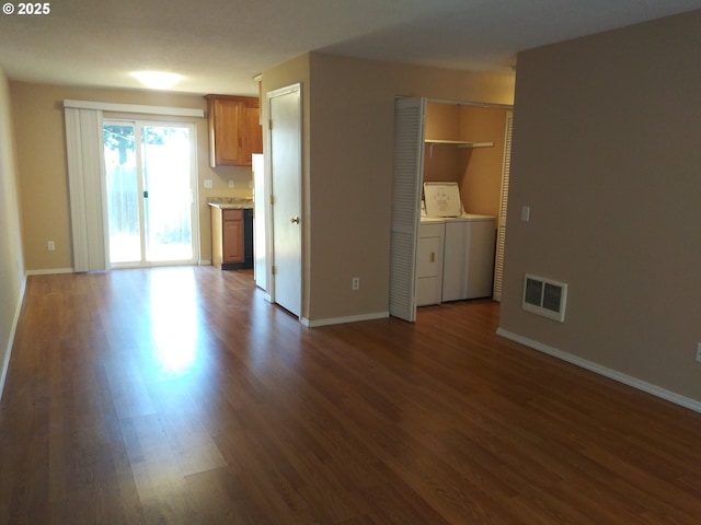 unfurnished living room with dark wood-style floors, baseboards, visible vents, and washing machine and clothes dryer