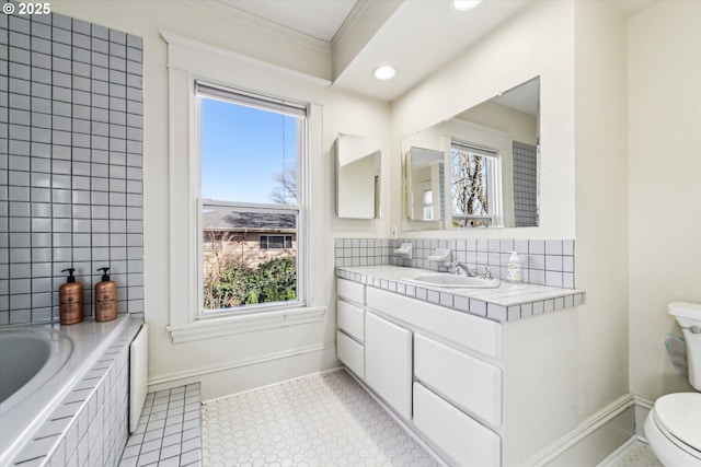 bathroom featuring a relaxing tiled tub, baseboards, decorative backsplash, toilet, and vanity