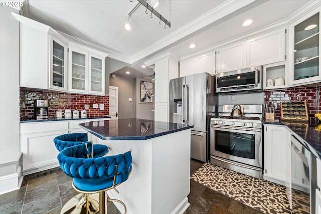 kitchen with stone tile floors, appliances with stainless steel finishes, white cabinets, and ornamental molding