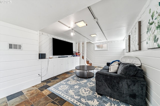 living room with wooden walls, visible vents, stone finish floor, stairway, and rail lighting