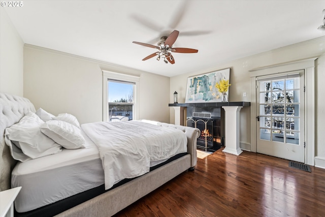 bedroom featuring ceiling fan, a lit fireplace, wood finished floors, and crown molding