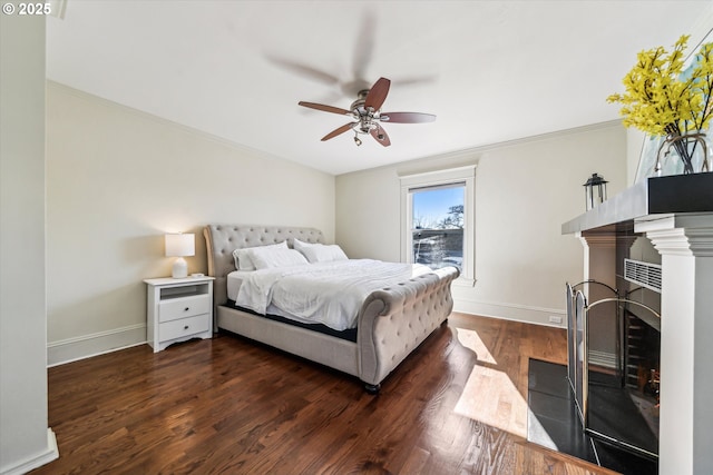 bedroom with ceiling fan, a fireplace with flush hearth, baseboards, dark wood finished floors, and crown molding