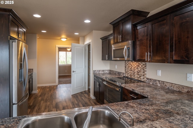 kitchen with dark wood-type flooring, a sink, backsplash, dark brown cabinetry, and appliances with stainless steel finishes