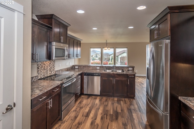 kitchen featuring dark brown cabinets, appliances with stainless steel finishes, a peninsula, an inviting chandelier, and a sink