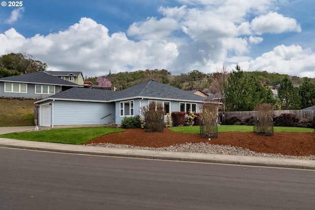 ranch-style home with a front lawn, fence, concrete driveway, an attached garage, and a shingled roof