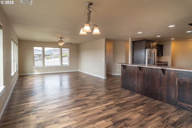 kitchen featuring light stone counters, recessed lighting, stainless steel fridge, a breakfast bar area, and dark wood-style flooring