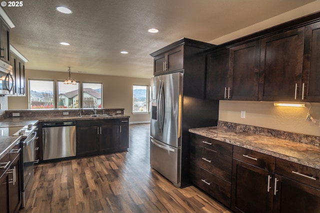 kitchen with dark wood finished floors, dark brown cabinetry, a chandelier, appliances with stainless steel finishes, and a sink