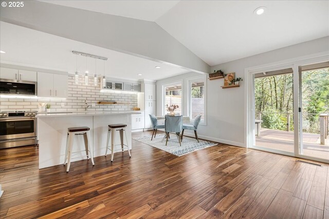 kitchen with stainless steel appliances, light countertops, glass insert cabinets, white cabinets, and a kitchen breakfast bar