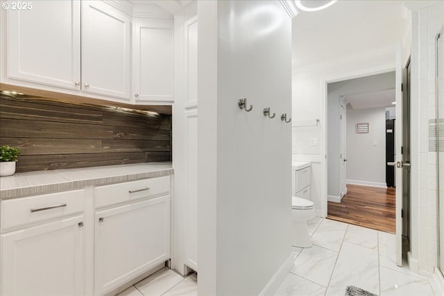 interior space with baseboards, toilet, a shower with shower door, marble finish floor, and vanity