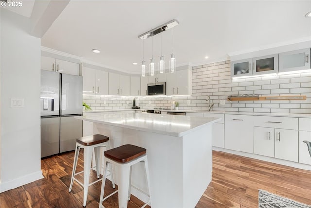 kitchen featuring stainless steel appliances, a kitchen island, white cabinets, glass insert cabinets, and pendant lighting