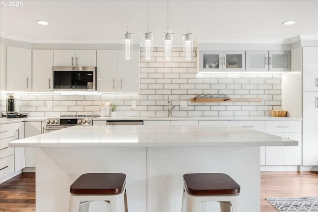 kitchen featuring light stone countertops, white cabinetry, appliances with stainless steel finishes, and glass insert cabinets