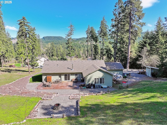 back of house with a patio area, a yard, and a forest view