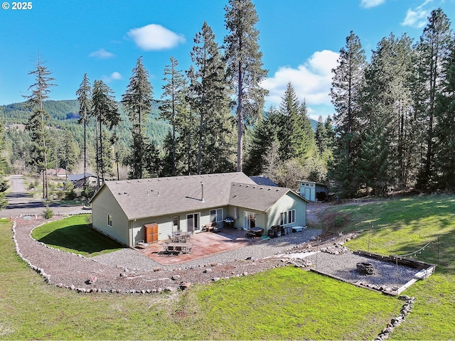 back of house featuring a wooded view, a patio, and a yard