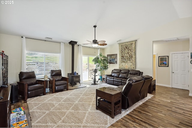 living room with visible vents, a wood stove, ceiling fan, and wood finished floors