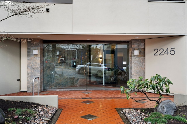 doorway to property featuring stone siding, stucco siding, and a patio