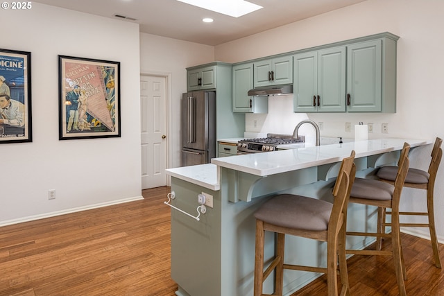 kitchen featuring a skylight, a kitchen bar, kitchen peninsula, stainless steel appliances, and light hardwood / wood-style flooring