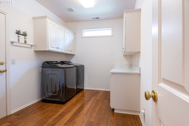 clothes washing area with separate washer and dryer, dark wood-type flooring, and cabinets