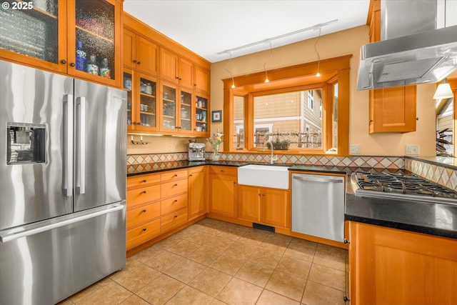 kitchen featuring exhaust hood, light tile patterned flooring, appliances with stainless steel finishes, a sink, and tasteful backsplash