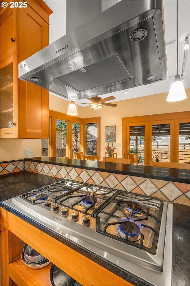 interior space featuring dark countertops, glass insert cabinets, brown cabinets, exhaust hood, and stainless steel gas stovetop