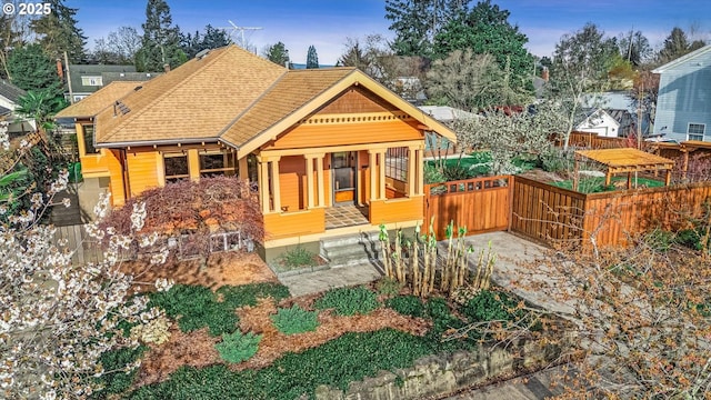 view of front facade with fence, a shingled roof, and a porch