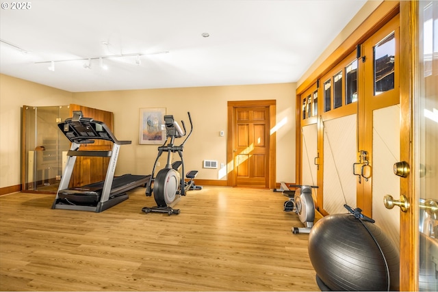exercise room with visible vents, baseboards, wood finished floors, and track lighting