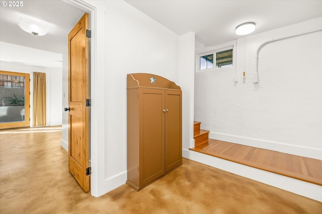hall featuring baseboards, stairway, and finished concrete flooring