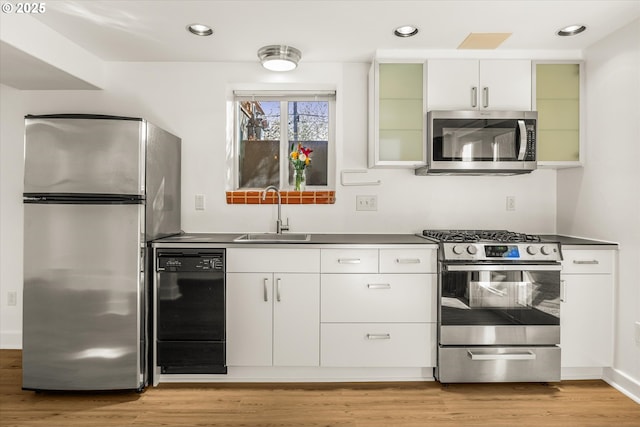 kitchen featuring glass insert cabinets, light wood-type flooring, white cabinetry, a sink, and appliances with stainless steel finishes