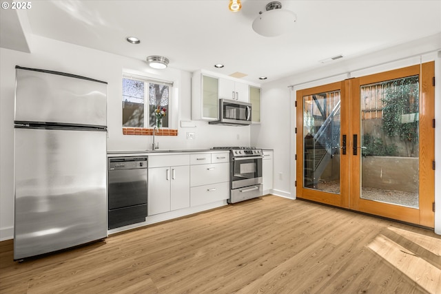 kitchen featuring visible vents, appliances with stainless steel finishes, a sink, light wood finished floors, and white cabinetry