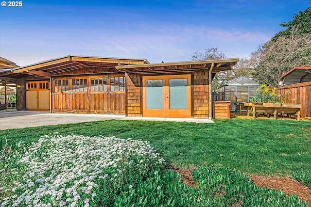 back of property featuring a lawn, an outdoor structure, fence, and a greenhouse