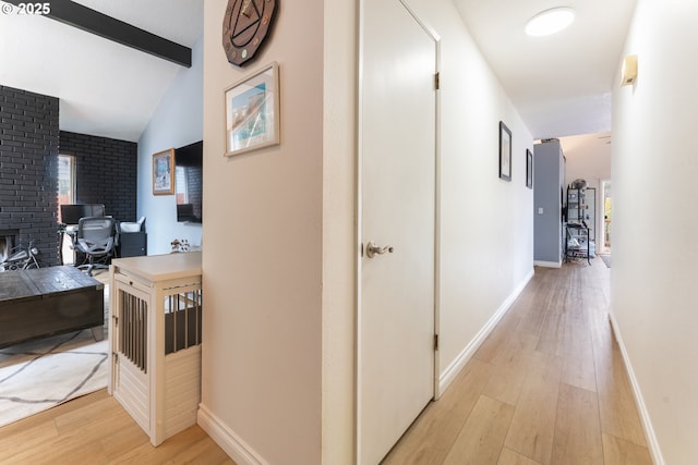 hallway with lofted ceiling with beams, baseboards, and light wood finished floors