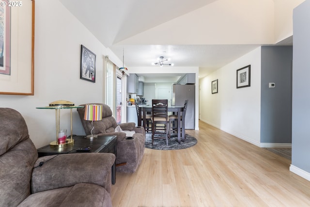 living area featuring lofted ceiling, light wood-style floors, and baseboards