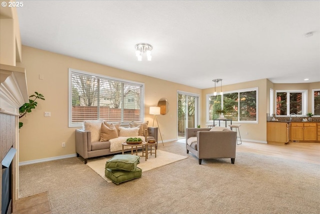 living area featuring baseboards, a fireplace with flush hearth, and light carpet