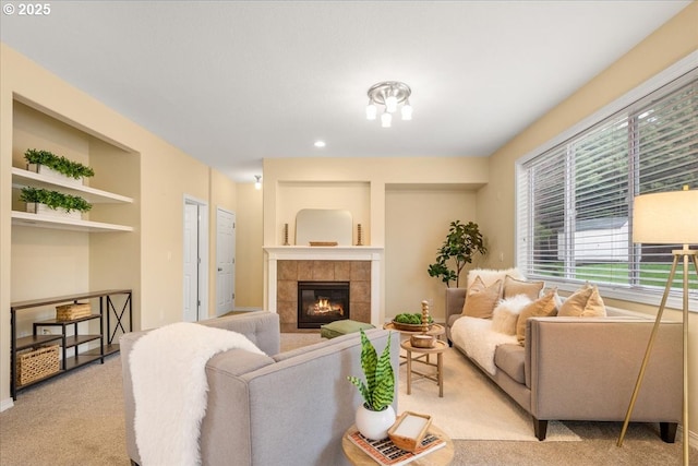 living area with a tiled fireplace, built in features, and carpet