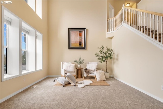 living area featuring carpet flooring, a healthy amount of sunlight, baseboards, and a towering ceiling