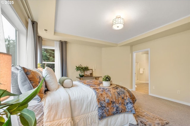 carpeted bedroom featuring a tray ceiling, baseboards, visible vents, and ensuite bathroom